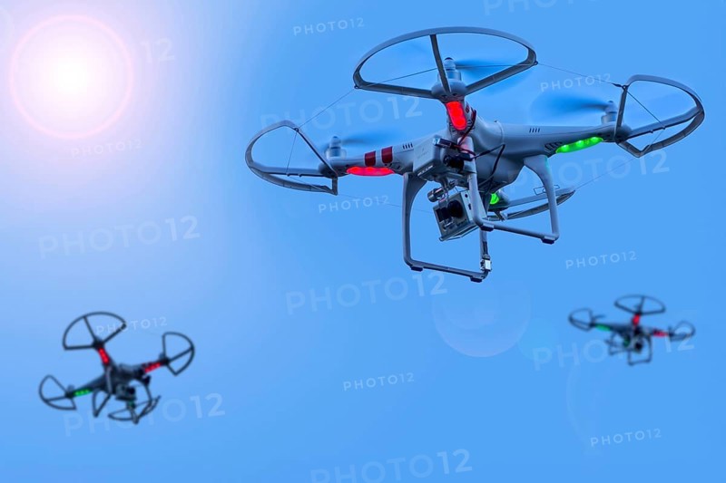 Three miniature quadcopter drones, teleoperated unmanned aerial vehicles, UAV equipped with cameras for aerial photography in flight in group. Digital composite. Sun digitally added