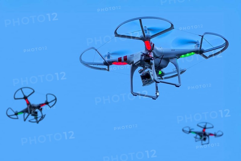 Three miniature quadcopter drones, teleoperated unmanned aerial vehicles, UAV equipped with cameras for aerial photography in flight in group. Digital composite