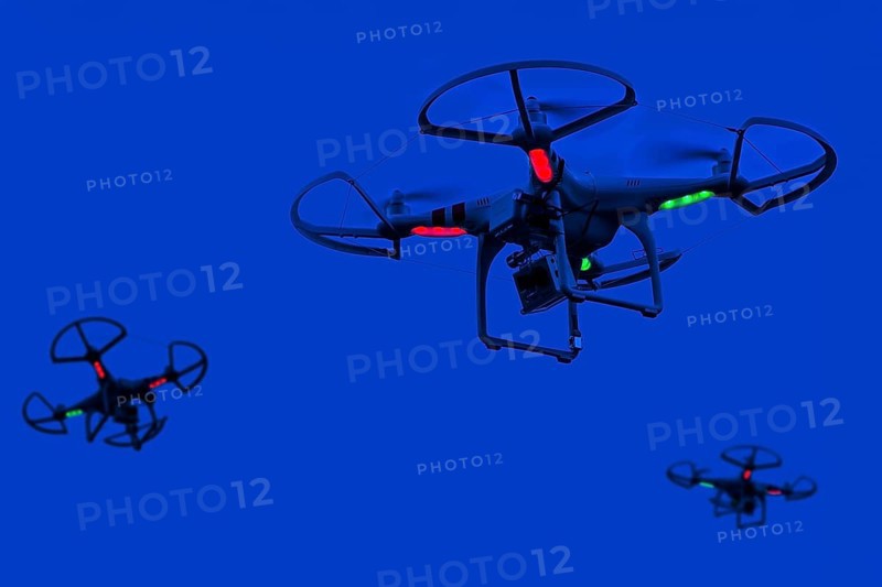 Three illuminated miniature quadcopter drones, teleoperated unmanned aerial vehicles, UAV equipped with cameras for aerial photography in flight at night. Digital composite