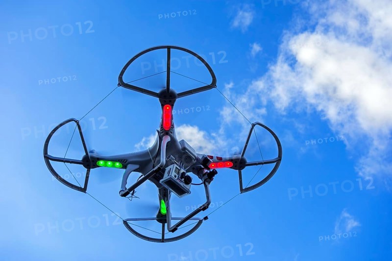 Miniature quadcopter drone, teleoperated unmanned aerial vehicle, UAV equipped with camera for aerial photography in flight against blue sky
