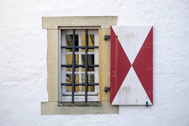Window with red and white shutters and iron bars in front of a white wall, Münsterland, North Rhine-Westphalia, Germany
