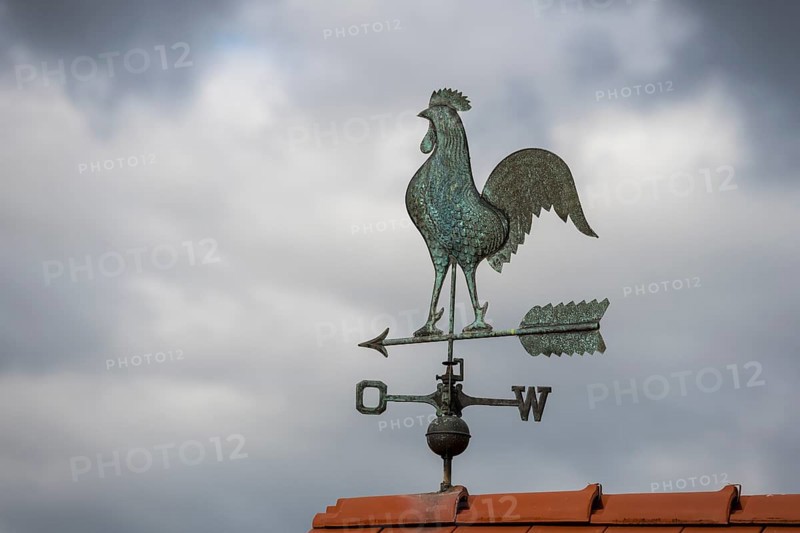 Rooster weather vane on a tiled roof against a dark cloudy sky, Baden-Württemberg, Germany