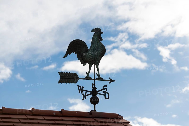Metal weather vane on a roof surrounded by blue sky and clouds, Baden-Württemberg, Germany