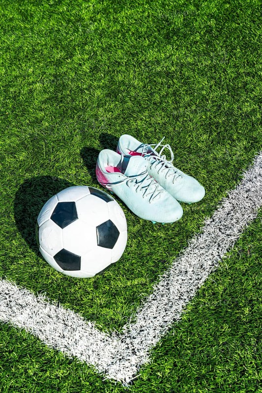 Soccer ball on artificial green turf beside light blue cleats and white boundary line, close top view evoking training, competition, preparation and active outdoor play