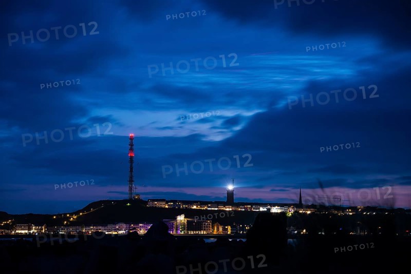 Panoramic view, view of the highlands of the island of Heligoland at night with red-lit radio tower, radio tower, transmitter, bright lighthouse, dark church tower and deep blue sky with lots of clouds above, nighttime lowland in front of it, rest of sunset in the night sky, quiet and dark atmosphere, cloud bank, weather, summer, night shot, long exposure, beacon, maritime, North Sea, Pinneberg district, Schleswig-Holstein, Germany