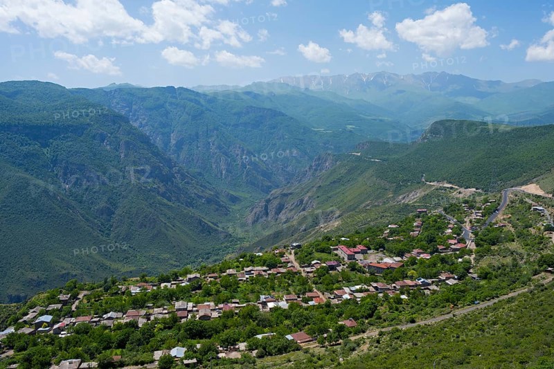 A small village is situated in a green valley surrounded by forested mountains under a cloudy sky, Halidzor, view from Wings of Tatev, Syunik province, Caucasus, Armenia