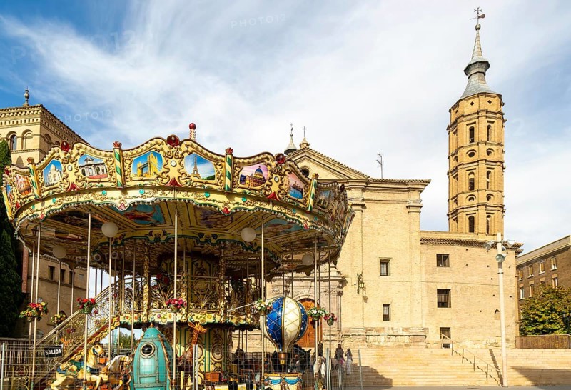 Funfair merry-go-round next to Church of San Juan de los Panetes with its Mudéjar tower, Zaragoza, Aragon, Spain