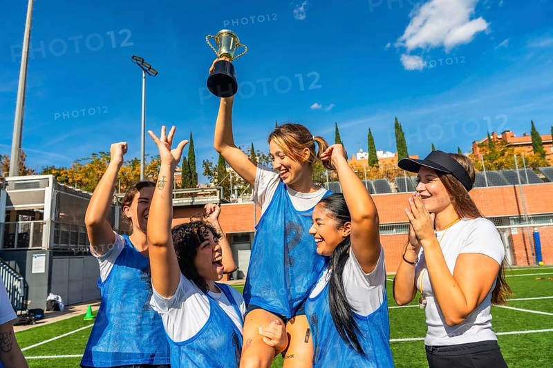 Happy young women soccer players celebrating victory on a sunny outdoor field, lifting the championship trophy together with smiles, teamwork and energetic joy after the win