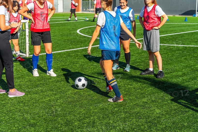 Diverse women soccer players training together on a sunny outdoor turf field, practicing dribbling, passing and teamwork to build fitness, skill and competitive confidence