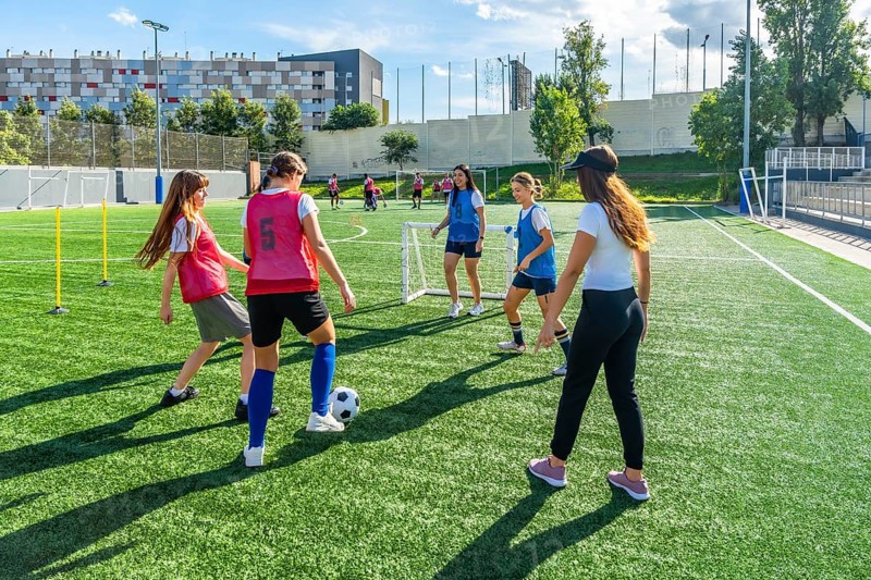 Female soccer teammates training on a sunny artificial turf field, practicing dribbling, passing and teamwork in an energetic outdoor session promoting fitness and youth sport development
