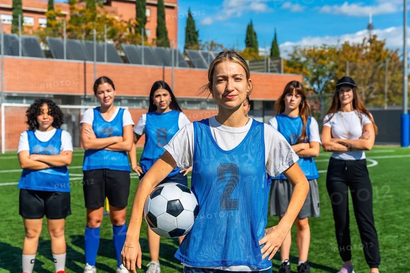 Diverse group of confident young women forming a soccer team, standing together on a green football pitch after a training session, showing unity and determination for their sport