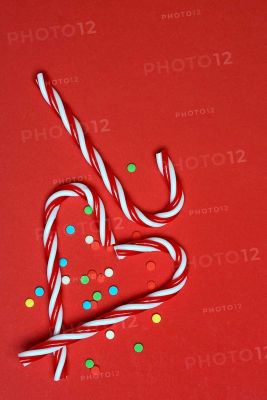 Candy canes and sugar confetti against red background, Christmas