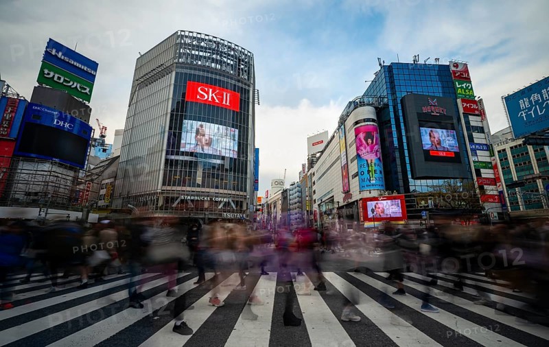 Crowd crossing zebra crossings on a large intersection, motion blur, modern houses with colorful neon signs at the back, long exposure Hibuya Crossing, Shibuya, Tokyo, Japan