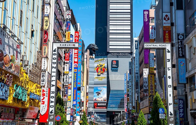 Bustling street scene in Japan with modern buildings and colorful billboards, figure of Godzilla head on a high-rise building, Shinjuku City, Tokyo, Japan