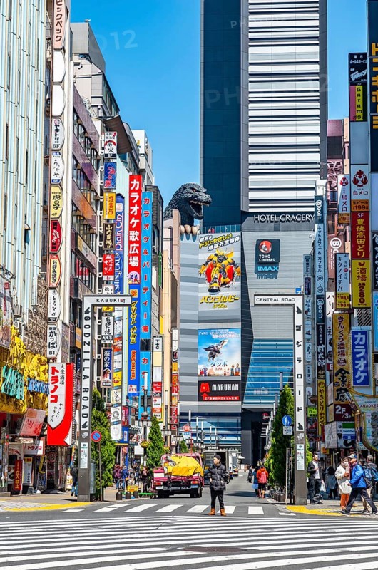 Bustling street scene in Japan with modern buildings and colorful billboards, figure of Godzilla head on a high-rise building, Shinjuku City, Tokyo, Japan