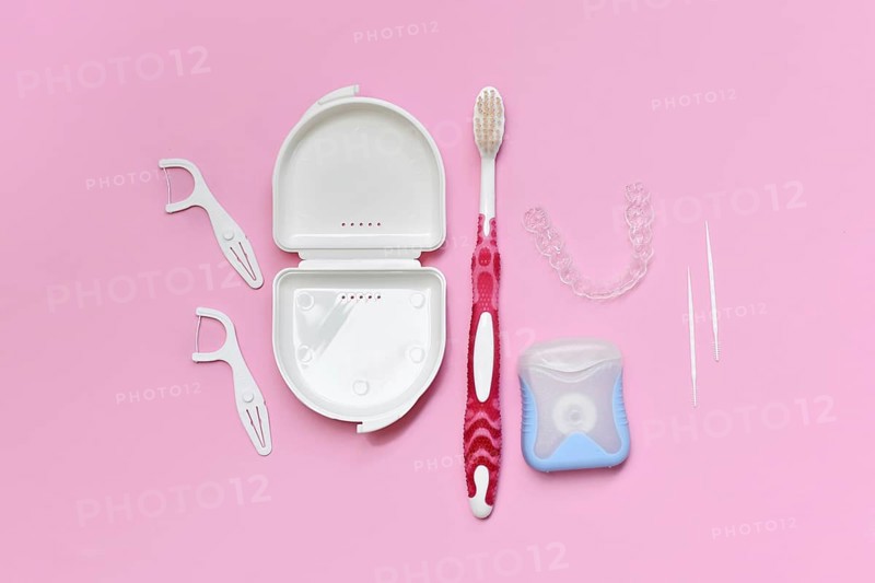 Top view of dental clear aligners, toothbrush, toothpicks and floss on pink background with copy space