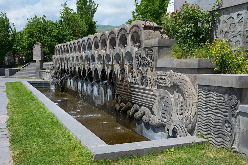 Stone fountain with sculptures surrounded by plants in bright weather, monument to the 40th anniversary of the victory in the Great Patriotic War, Sisian, Sisian, Syunik province, historically Sangesur, Armenia