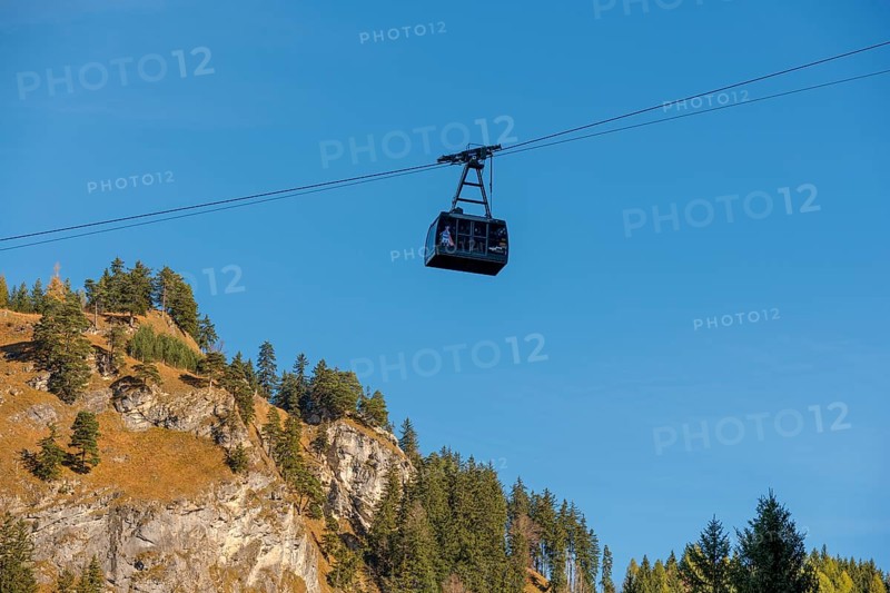 A Tegelbergbahn cabin floats over a mountainous landscape under a clear blue sky, near Schwangau, Ostallgäu, Allgäu, Bavaria, Germany