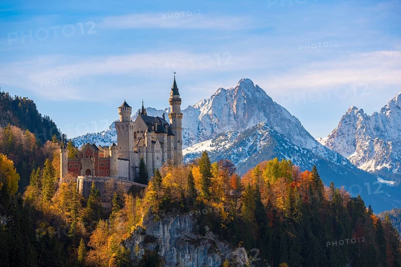 Neuschwanstein Castle rises impressively against a snowy mountain backdrop, surrounded by autumnal forest, Schwangau near Füssen, Ostallgäu, Allgäu, Bavaria, Germany