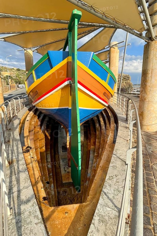 Monument to traditional fishing boats abandoned jacked up typical colorful painted old fishing boat with large rudder blade at the stern of Gozo at Gozo harbour, Mgarr Harbour, Gozo, Malta