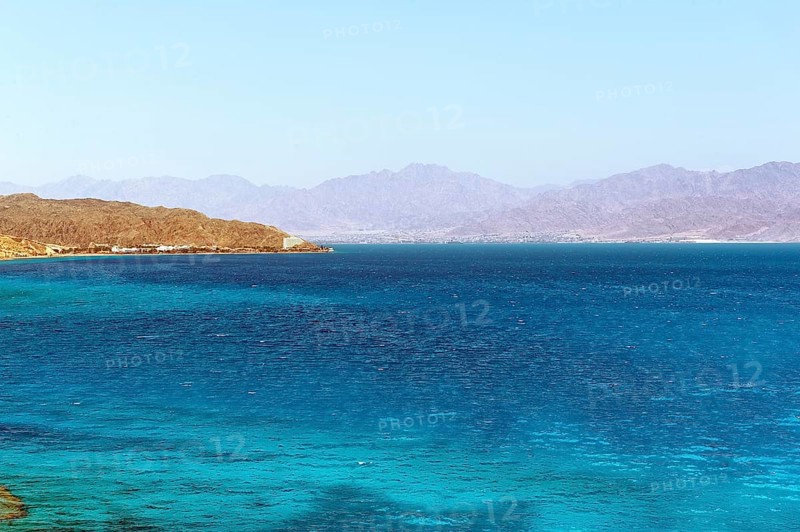 View of the Egyptian coast from the Sinai peninsula not far from the border with Israel across turquoise blue water from in the Gulf of Aqaba Red Sea on the Jordan coast with a small city of Aqaba in the background, Egypt, Jordan