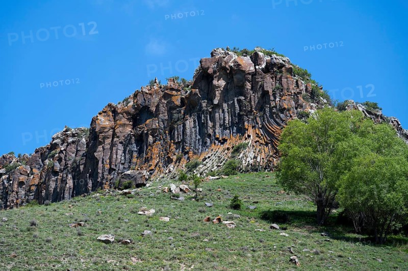 Mighty rock formation with lush greenery and clear skies, radiating peace and natural beauty, basalt columns near Shaki Waterfall, Syunik Province, Armenia