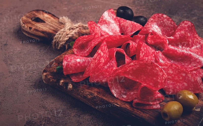 Sliced salami sausage, on a wooden chopping board, decorated with olives and herbs, close-up, no people