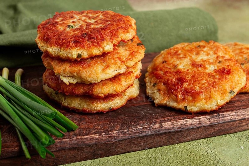 Crispy potato pancakes Latkes, stacked on a wooden board next to fresh green onions, natural light, homemade, no people
