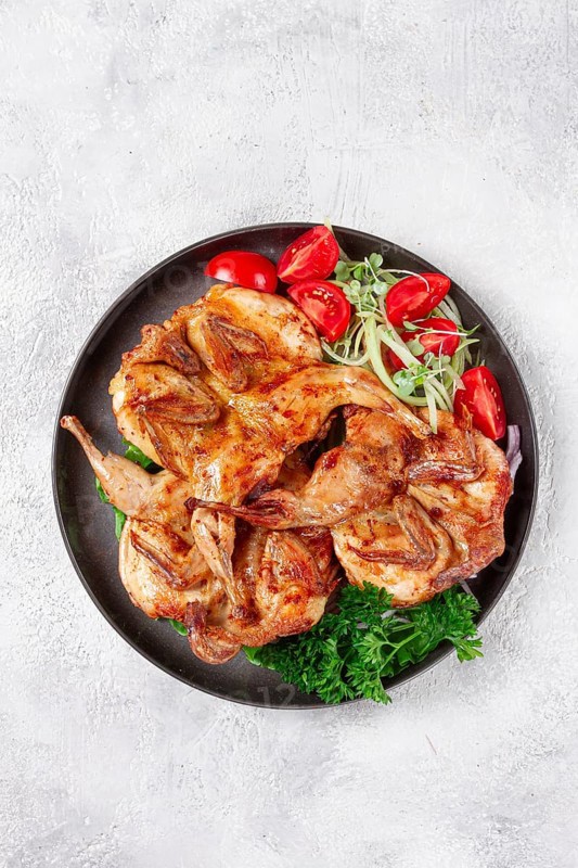 Baked quail, served on a plate with crispy lettuce leaves, fresh tomatoes and herbs, on a dark plate, homemade