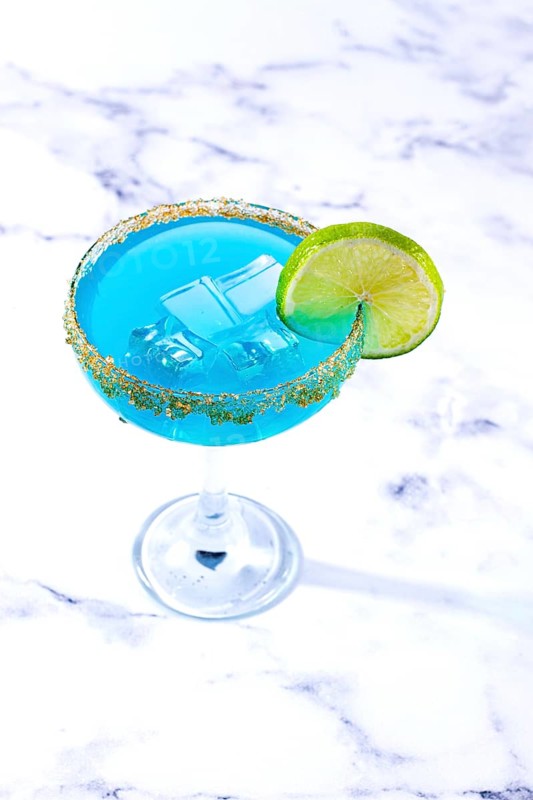 Bright blue cocktail with a slice of lime on a marble surface