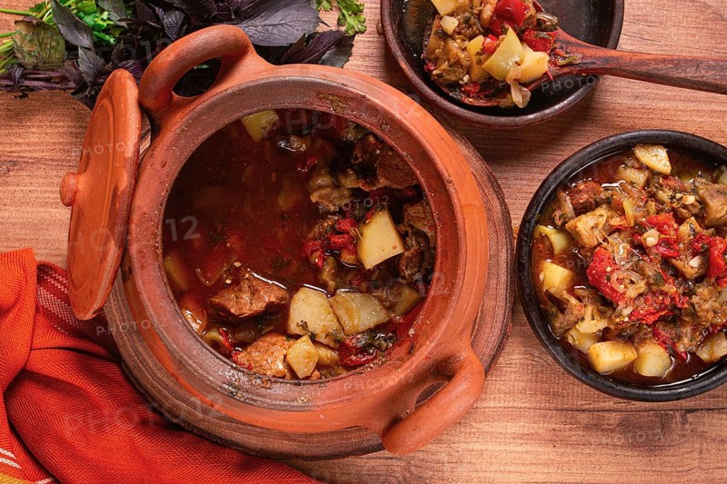 Chanakhi, a Georgian dish. in a clay pot, on a wooden table, stewed meat with vegetables, homemade, no people