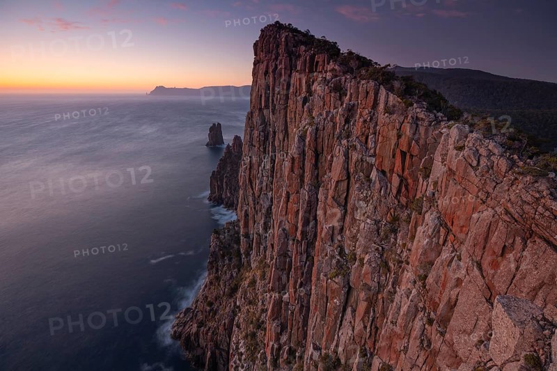 Long exposure at sunrise shows the glowing dawn over the huge rocks of Cape Hauy. Waves hit the steep cliffs. Cape Hauy, Tasman Peninsula, Tasmania, Australia