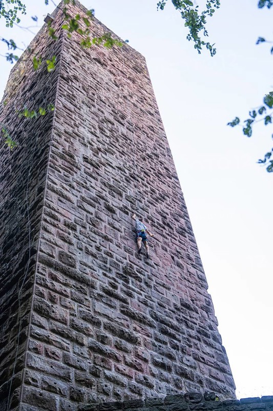 A climber climbs the stone wall of a tower, accentuated by clear air and natural surroundings, Mandelberg Castle Ruins, Pfalzgrafenweiler, Freudenstadt District, Germany