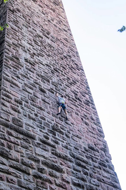 A climber climbs a massive stone tower surrounded by trees and blue sky, Mandelberg Castle Ruins, Pfalzgrafenweiler, Freudenstadt District, Germany
