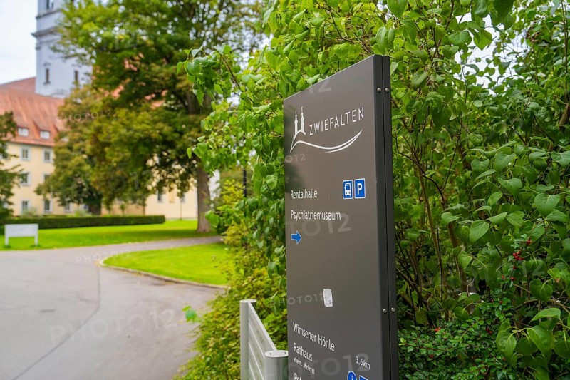A sign with the reference to Zwiefalten stands against a background of green plants and a building, ZFP Zwiefalten, Reutlingen district, Germany