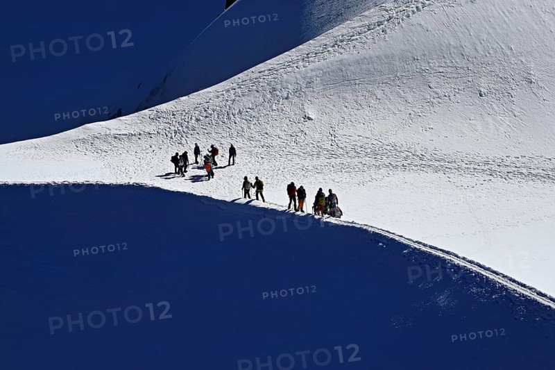A group of mountaineers runs across a snow-covered mountain ridge, Aiguille du Midi, Chamonix-Mont-Blanc, Haute-Savoie, France