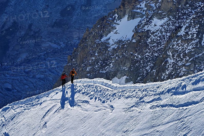 Two ascended mountaineers run across a snow-covered mountain ridge, Aiguille du Midi, Chamonix-Mont-Blanc, Haute-Savoie, France