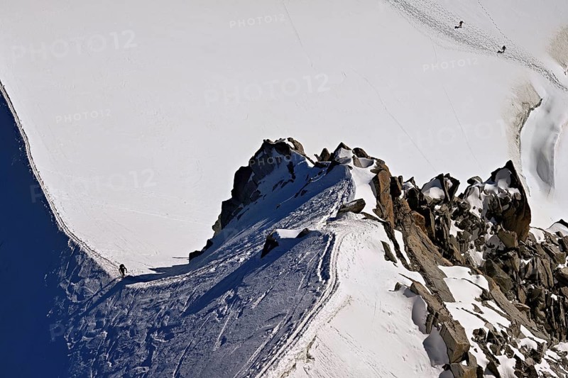 A mountaineer climbs over a snow-covered mountain ridge, Aiguille du Midi, Chamonix-Mont-Blanc, Haute-Savoie, France
