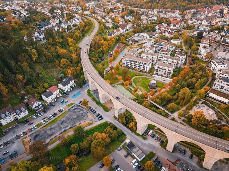 Aerial view of a city with a curved bridge surrounded by autumn trees and residential buildings, Nagold, Black Forest, Germany