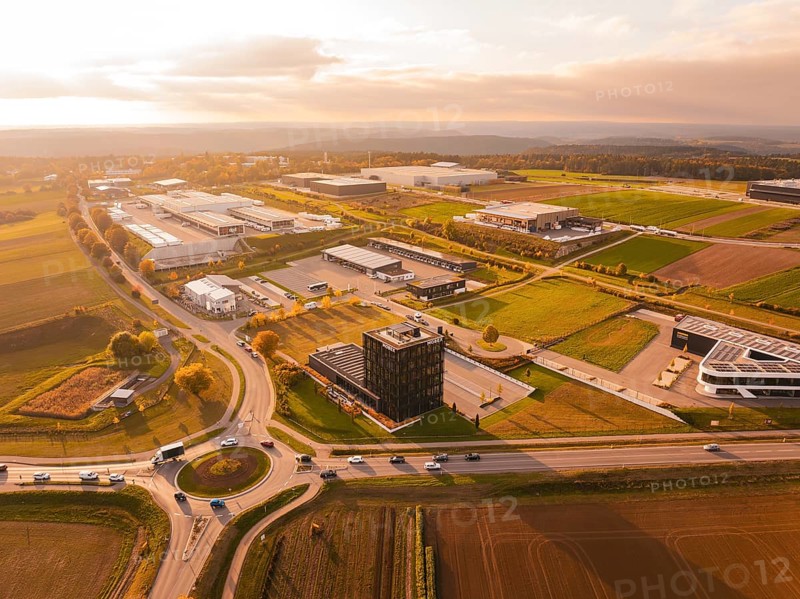 Large Mobex industrial plants surrounded by fields and road networks shine in warm evening light, Nagold, Black Forest, Germany