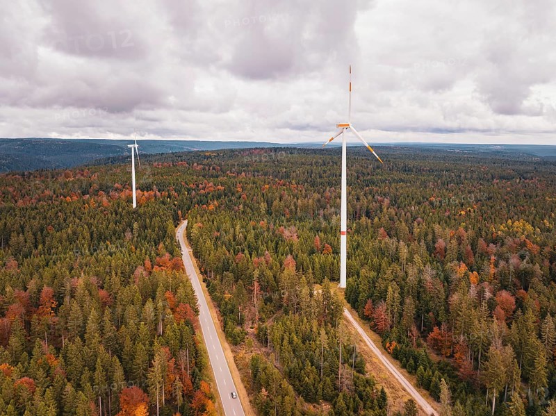 Wind turbines in colorful autumn forest with road under cloudy sky, Simmersfeld wind farm, Germany