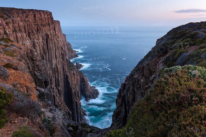 The Gap with long exposure shows the sunset over the cliffs of Cape Raoul. Golden light hits the sea and colors the rocks warmly in the evening. Cape Raoul, Tasman Peninsula, Tasmania, Australia