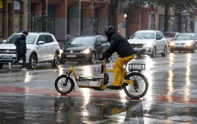 A man rides a cargo bike across a rained road in heavy rain, Berlin, 30.10.2025, Berlin, Berlin, Germany