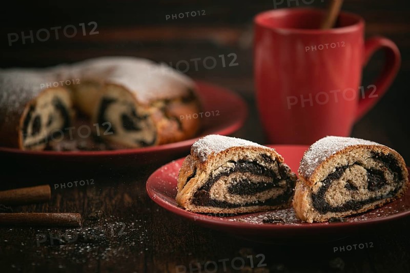 Poppy seed cake with red crockery and cinnamon sticks on wooden background