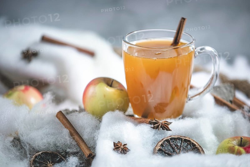 A glass of apple punch with cinnamon sticks and apples in a winter environment