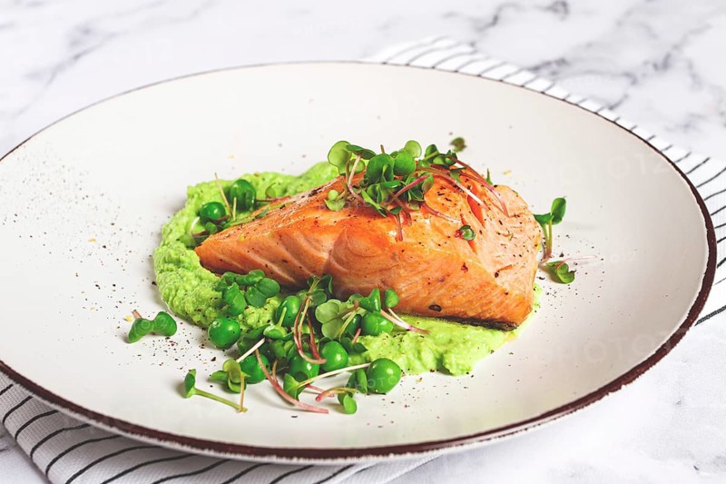 Delicious grilled salmon is placed elegantly on creamy green pea puree. Fresh microgreens and peas add a bright touch, creating an appetizing dish perfect for any meal