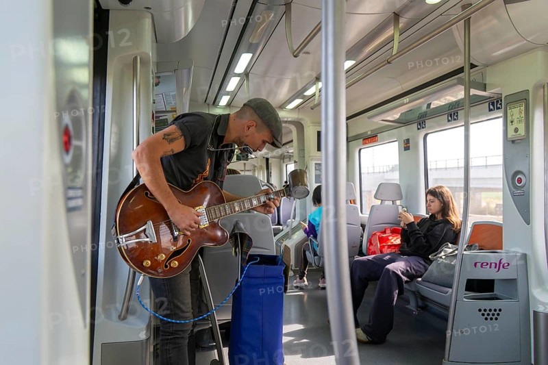 Musician busker playing guitar onboard train of Rodalia de Barcelona suburban rail network, Barcelona, Catalonia, Spain