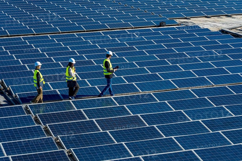 Engineers wearing safety vests and hard hats walking along rows of blue solar panels, performing inspection and maintenance at a renewable energy power station