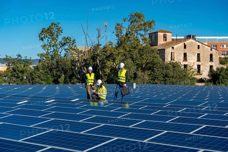 Three engineers wearing safety helmets and vests performing an inspection of a large rooftop solar panel installation, ensuring efficient operation and maintenance of the sustainable energy system