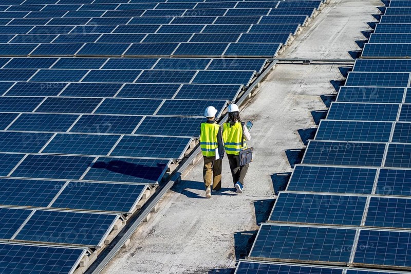 Engineers wearing safety helmets and vests assessing the performance of solar panels on a large solar farm, focusing on sustainable energy and green power development